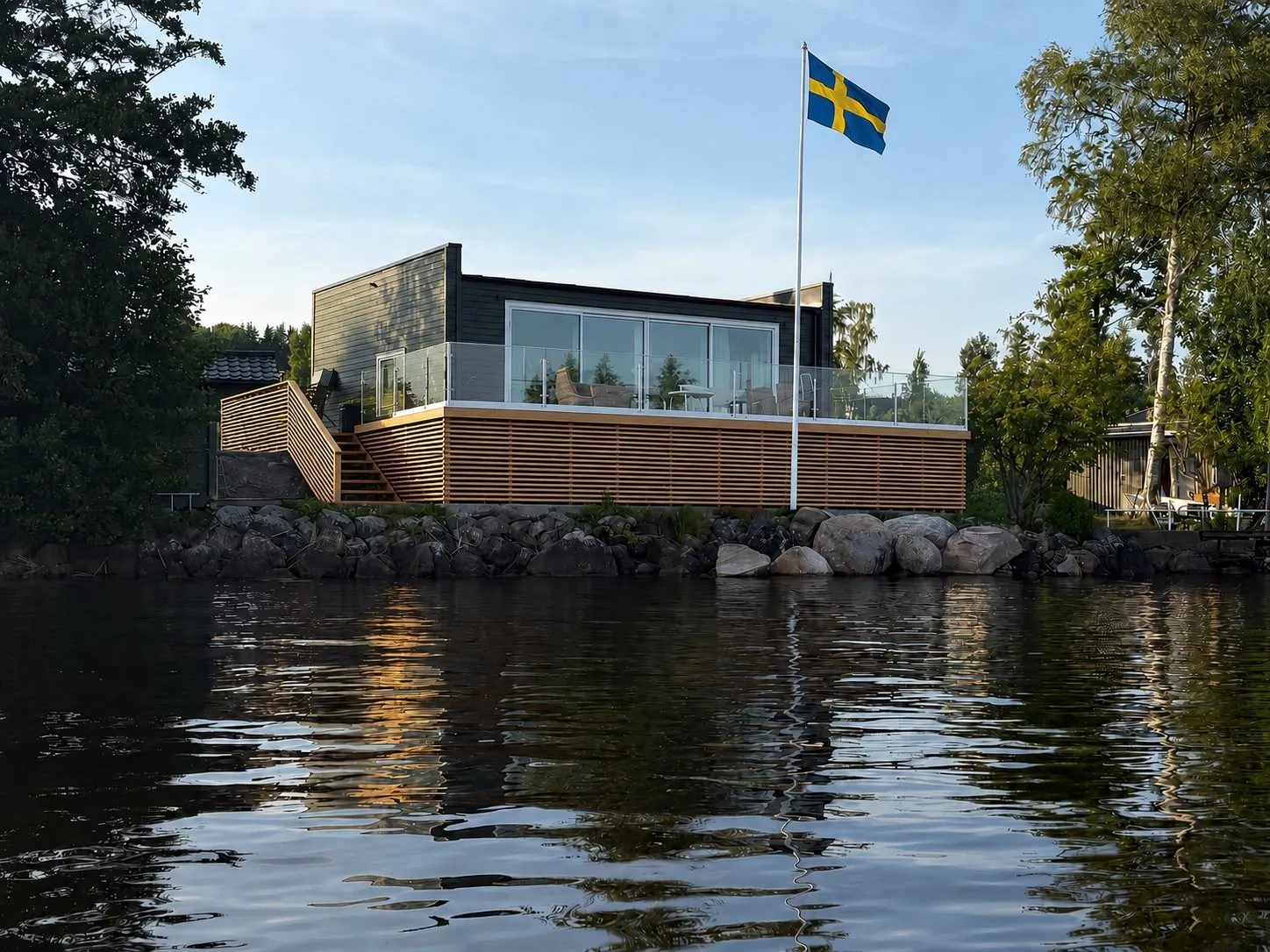 Nybyggt fritidshus vid sjön med altan och svensk flagga